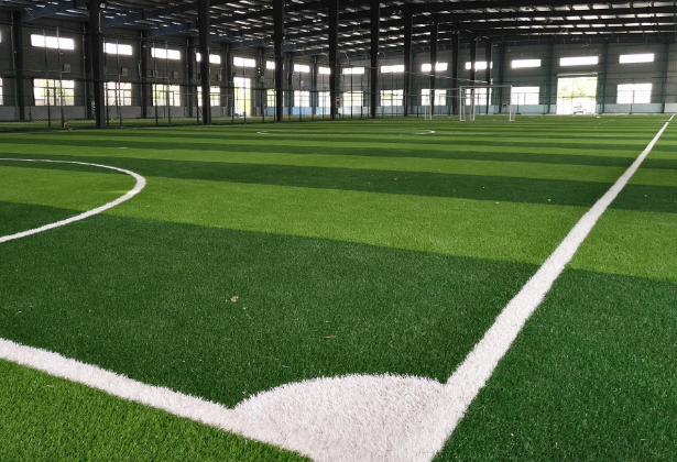 Indoor artificial turf soccer field with white boundary lines, striped green grass pattern, and a warehouse-style building around it, in a calm and orderly mood